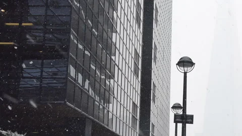 Snow falling down on the street with a glass office building. Stock Footage
