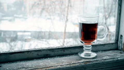Snow falling on glass cup with tea on window sill Stock Footage 71218243