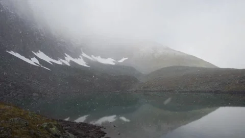 Snow is falling on a mountain lake. Rocks and mountain in the background Video stock 161534331