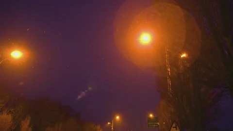 Snow falling at night illuminated by bright orange street lamps on a highway Video stock 342112461