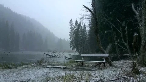 Snow is falling over a bench near a lake Stock Footage 77017341