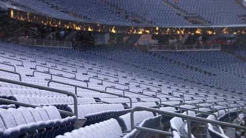 Snow falling over empty seats in football stadium with flames on video screen Stock Footage 104773605