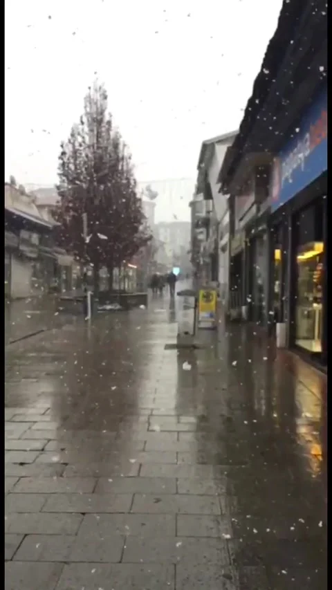 Snow falling over a quiet city street with shops and trees during winter, Vídeos de archivo 333240924