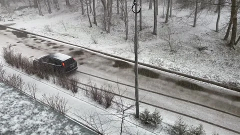 Snow is falling on the road on which the black car is driving. Video stock 262046324