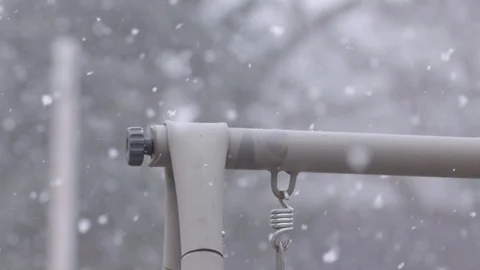 Snow falling in slow motion on a sunny day with a metal frame in focus. Stock Footage 88683723