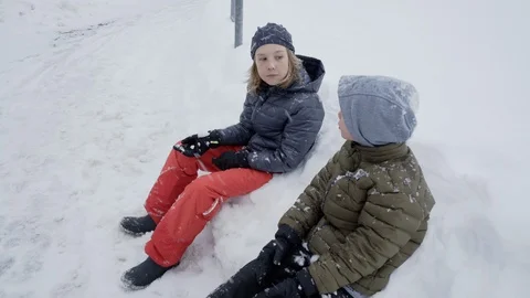Snow falling on two boys chatting while sitting on snowbank in Germany Stock Footage 120984086