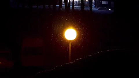 Snow falling under glowing streetlamp at night Stock Footage 323112464