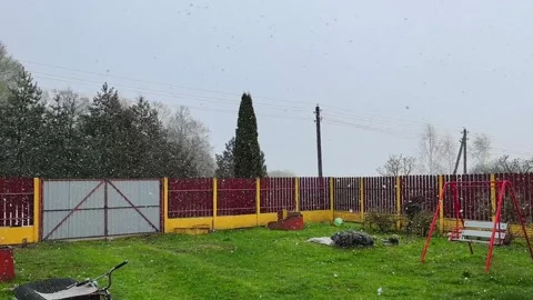 Snow falls in a backyard with a swing set on a gray day in spring Stock Footage 339008037