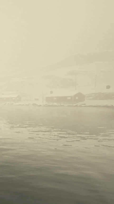 Snow falls over a quiet harbor with cabins on a foggy day in winter Stock Footage 339098951