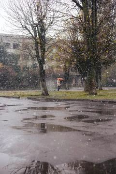 Snow falls on a rainy spring day with a person walking under an umbrella in.. Stock Photos