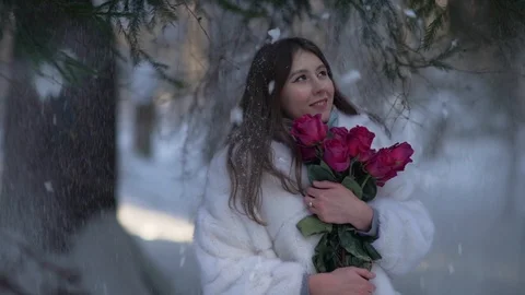 Snow falls on young beatiful smiling woman with roses in winter forest	 库存影片 102176714