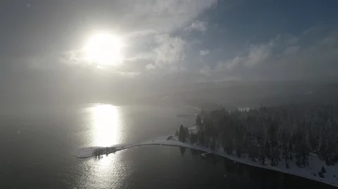 Snow flakes falling with the sun shining over lake tahoe aerial view Stock Footage 98499497