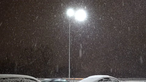 Snow flakes fly in the light of a lantern and moving cars in 4K Stock Footage 141820169