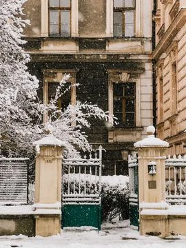Snow gently falling on elegant building facade, highlighting wrought iron gate Stock Photos