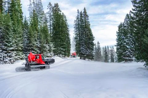 Snow groomers on alpine road through forest Stock Photos
