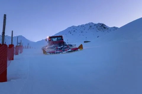 Snow grooming machine preparing a ski slope in twilight. Winter ski resort La Stock Photos