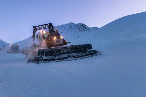 Snow grooming machine preparing a ski slope in twilight. Winter ski resort La Stock Photos
