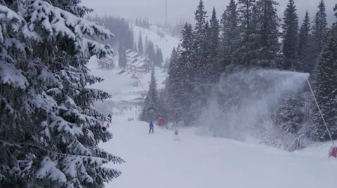 Snow gun between trees making snow for ski resort on cloudy day with snowfall 스톡 동영상 64921488
