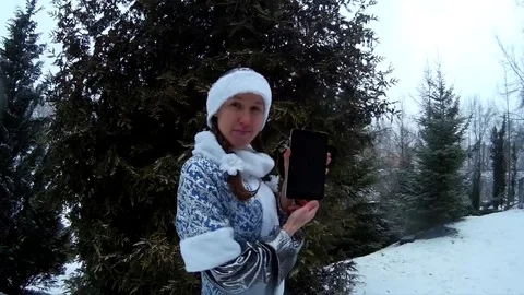 Snow Maiden in forest shows tablet computer in front of firm pine tree smiling Video stock 71016101