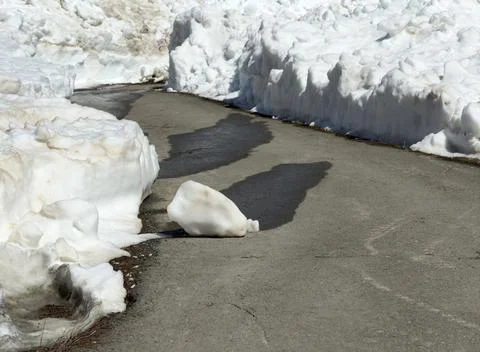 Snow melts on paved road, creating dark puddles 库存照片