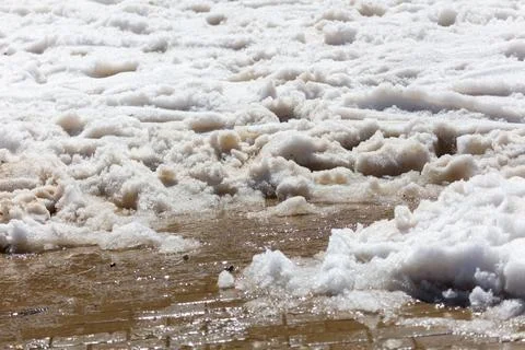Snow melts on wet sand, creating muddy puddles 库存照片