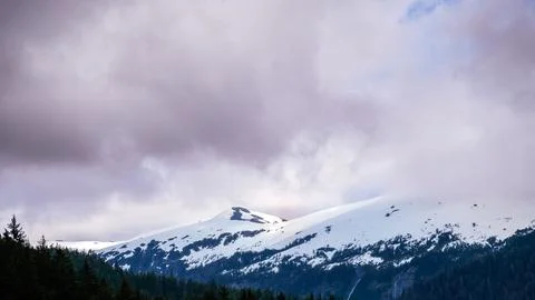 Snow on mountain tops with low clouds and shaded forest Fotos Stock