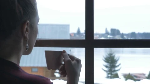 The snow outside the window and hot tea. Young woman with Cup of hot drink Stock Footage 70688129