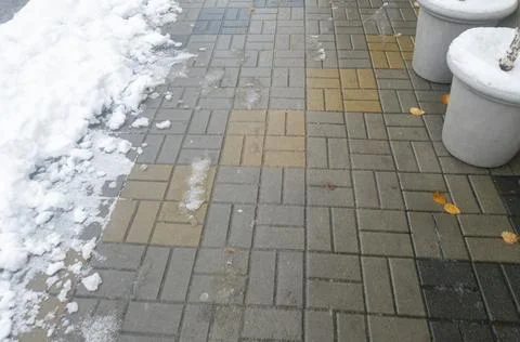 Snow partially covers a patterned sidewalk with rectangular tiles, featuring a Stock Photos
