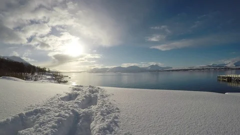 Snow patch with trail on small hill with golden sunshine and blue sky and fjord  Video stock 72951201