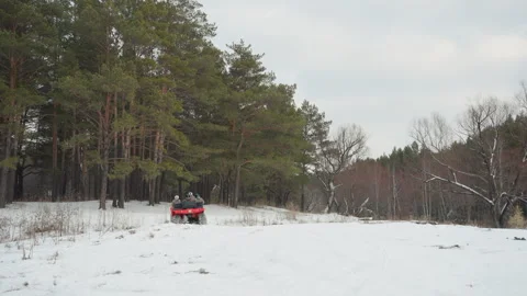 Snow quad adventure. Rider accelerates ATV over icy terrain with pine background Stock Footage 332169558