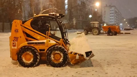Snow removal in progress: a yellow mini excavator with a bucket is actively Видео 327326956