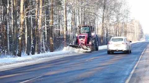 Snow removal on a road using a tractor in winter along a tree-lined area in the Vídeo Stock 328248665