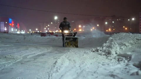 Snow removal with a snow thrower in the evening in an amusement park. A man Stock-Footage 168793041