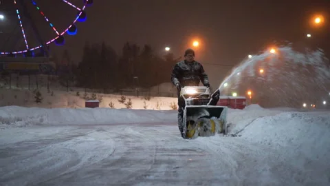 Snow removal with a snow thrower in the evening in an amusement park. A man Stock Footage 170372364