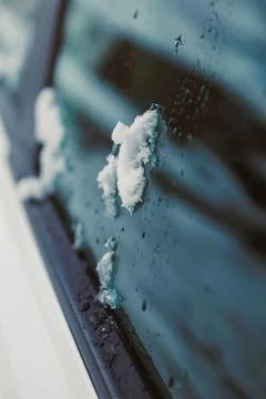 Snow rests on a car window while water droplets gather on the glass surface.. Stock Photos