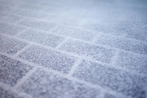 Snow rests lightly on a paved sidewalk surface. Square tiles form a regular.. Stock Photos