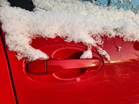 Snow rests on the side window and door handle of a red car Photos