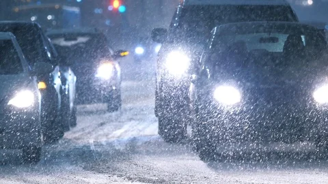 Snow storm in winter city, falling snow illuminated cars headlights. Slow motion Stock Footage