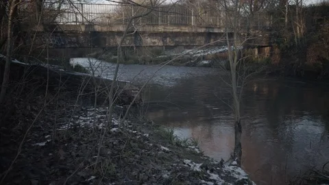 Snow thaw by a river in the winters evening flowing under a bridge Stock Footage 160779660