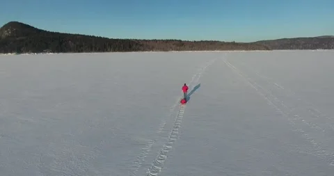 Snow trekker on a massive frozen river pulling toboggan aerial drone red Stock Footage 219956457