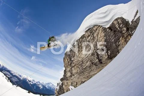 A Snowboarder Airs Off A Snow Pillow While On A Cat Ski Trip. Monashee