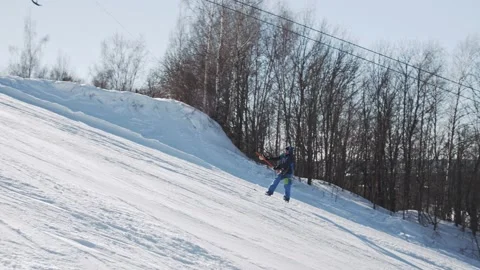 Snowboarder climbs using a T-bar lift and makes a buttering nose grab trick Video stock 221581716