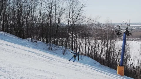 Snowboarder climbs using a T-bar lift and makes a buttering tail grab trick Stock Footage 221581792