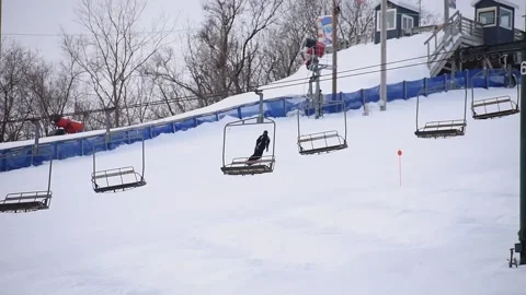 Snowboarder Going Down Snow-Covered Ski Hill, Chair Lift in Foreground Stock Footage 148706062