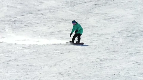 Snowboarder in a turquoise jacket gliding down a mountain. sunny day slow motion Vidéo 303093105