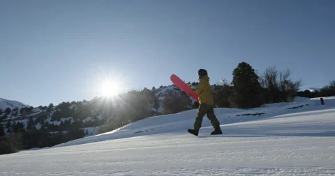 Snowboarder walking on an empty ski slope with snowboard in his hand in the Stock Footage 258188704