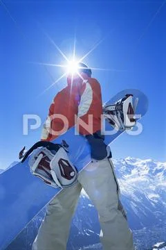 Snowboarder walking on snowy hill carrying board (lens flare) Stock Photos