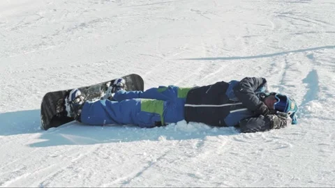 A snowboarder waves his mittened hand and lies down to sleep on the snow tired 動画素材 221581636