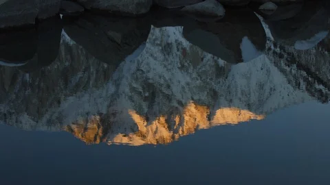 Snowcapped Mountain Reflection in Rippling Lake with Foreground Boulders Vídeo Stock 124555070