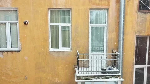 Snowfall Against Yellow Building Wall with Balcony and Windows Visible Stock Footage 325491883
